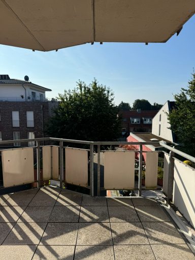 Balkon mit Sonnenschirm, Blick auf Nachbargebäude und Bäume im Hintergrund.