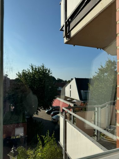 Blick von einem Balkon auf eine Straße mit Bäumen und Häusern im Hintergrund.