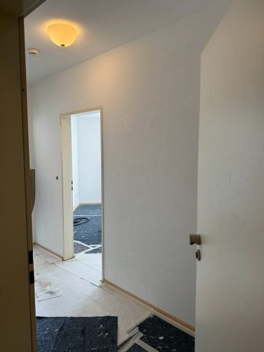 Blick in einen hellen Flur mit weißen Wänden und einer offenen Tür im Hintergrund.