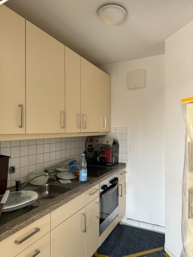 Kleine Küche mit hellen Schränken, Herd, Spüle und weißer Wand.